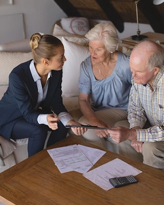 Three people discussing documents at a wooden table with a calculator present.
