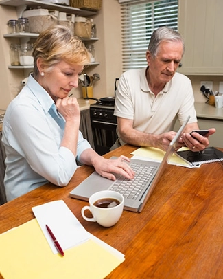 Senior couple planning finances with laptop and documents in kitchen.