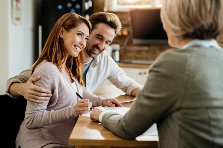 Young couple smiling while signing documents at a desk with advisor.